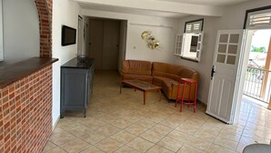 Un soggiorno con un divano in pelle marrone, un tavolino in vetro, uno sgabello rosso, una TV a muro e un camino in mattoni.