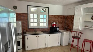 Una cucina compatta con mobili bianchi, un piano di lavoro nero, una pentola rossa su un fornello e due sgabelli rossi.