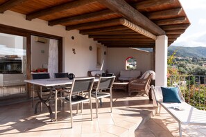 Une terrasse couverte avec une table et des chaises, un fauteuil de relaxation et une vue sur la campagne.