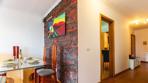 A dining area with a glass table, wooden chairs, a stone accent wall, and a colorful painting. - Sweet Home Reis Magos by Atlantic Holiday (Caniço)