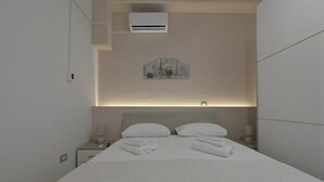 Ein modernes Hotelzimmer mit einem ordentlich bezogenen Bett, einem Nachttisch mit Lampe und einer wandmontierten Klimaanlage.