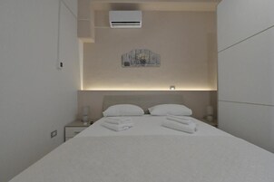 A modern hotel room with a neatly made bed, a bedside table with a lamp, and a wall-mounted air conditioner.