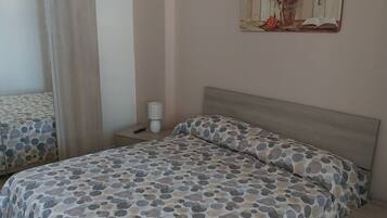 Un dormitorio con cama, mesita de noche, lámpara y espejo.