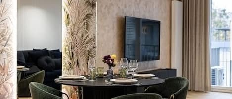 A modern dining area with a round table set for four, surrounded by green upholstered chairs.