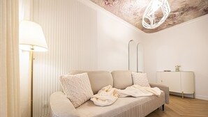 Ett modernt vardagsrum med en beige soffa, en golvlampa, ett vitt skåp och en dekorativ taklampa.