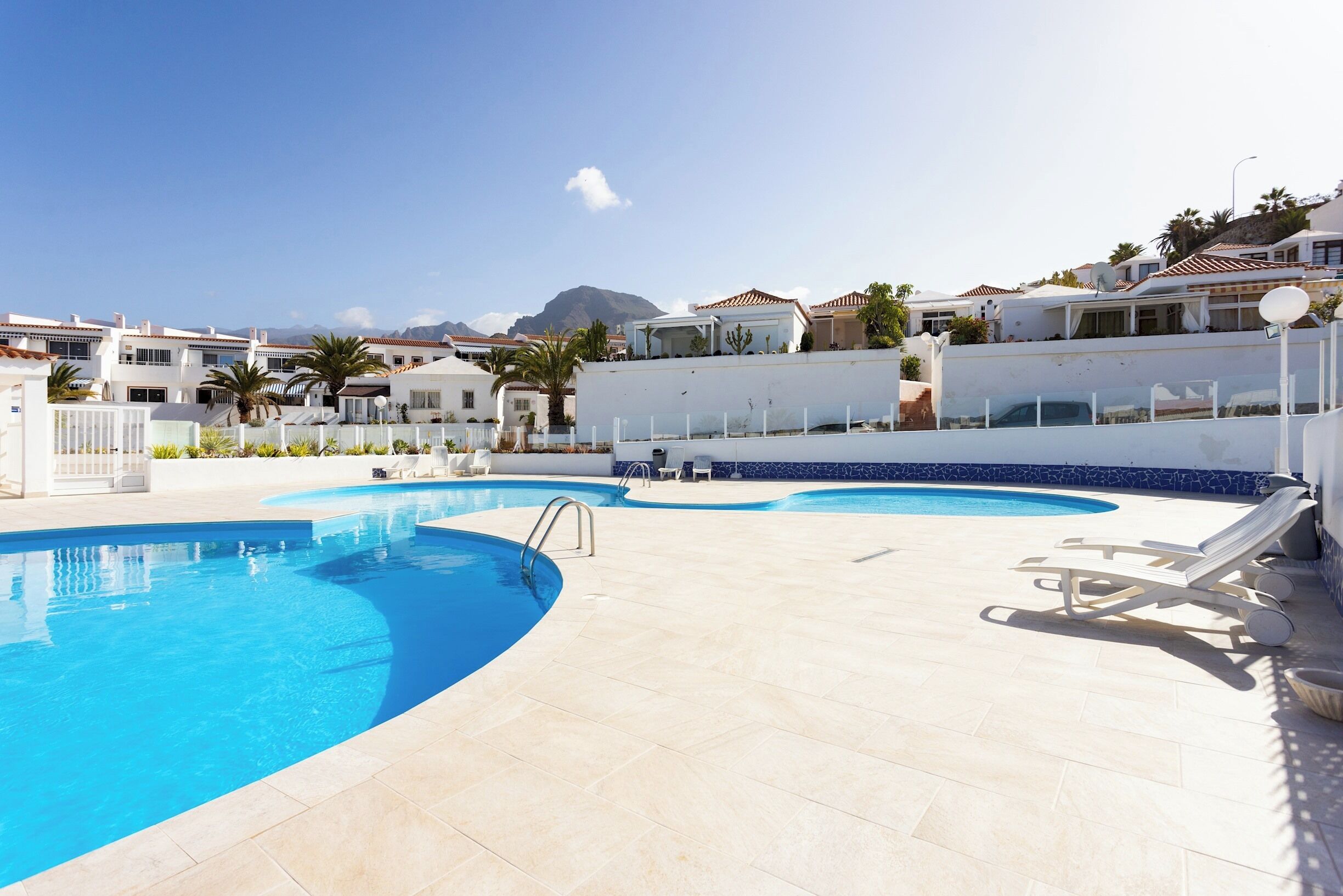 A swimming pool with a curved design, surrounded by lounge chairs and a white wall.