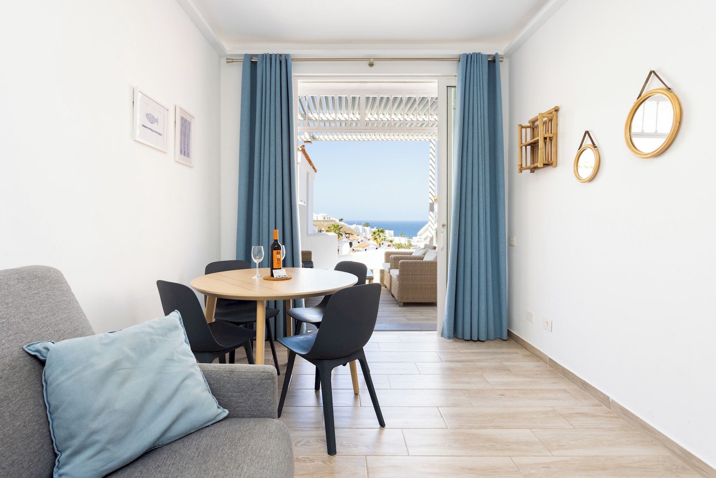 Una sala de estar moderna con comedor, vista al mar y un balcón con cortinas azules.