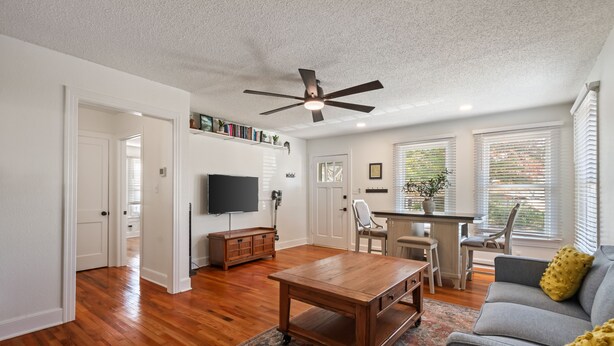 A spacious living room with hardwood floors, a ceiling fan, a grey sofa, and a coffee table. - 3BR in Crestview • 2 Kings • UT • Downtown • Events • Free Parking (Austin)