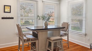 A dining area with a table and four chairs, white walls, and large windows with blinds. - 3BR in Crestview • 2 Kings • UT • Downtown • Events • Free Parking (Austin)
