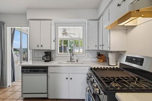 A modern kitchen with white cabinets, a built-in dishwasher, a stove, and a window with a view of the outdoors.