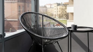 Une chaise moderne avec une structure en métal et une petite table sur laquelle se trouve une tasse, le tout placé près d’une fenêtre donnant sur des immeubles.