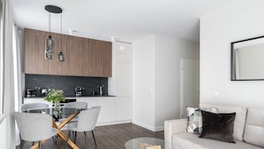 Une cuisine moderne avec des meubles en bois, un coin repas avec une table et des chaises en verre, et un salon avec un canapé et des coussins.