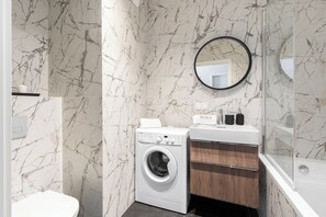 A modern bathroom with a marble wall, a washing machine, a sink, and a mirror.