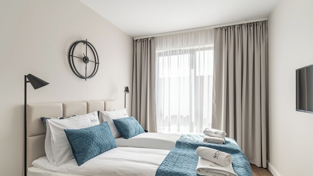 Une chambre d’hôtel moderne avec deux lits, une horloge murale ronde, une télévision et une grande fenêtre avec des rideaux.