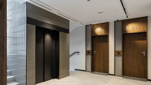 Un espace moderne avec deux ascenseurs, numérotés 24 et 25, et un escalier agrémenté d’un mur décoratif.