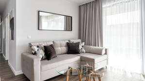 Un salon moderne avec un canapé d’angle beige, une table basse en verre et un grand miroir mural.