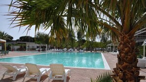 A swimming pool with lounge chairs and palm trees. - Happy Camp in Kamemi Camping Village (Ribera)