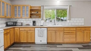 A modern kitchen with wooden cabinets, a built-in microwave, and a dishwasher. - Midnight Sun Viewpoint Aurora (Fairbanks)