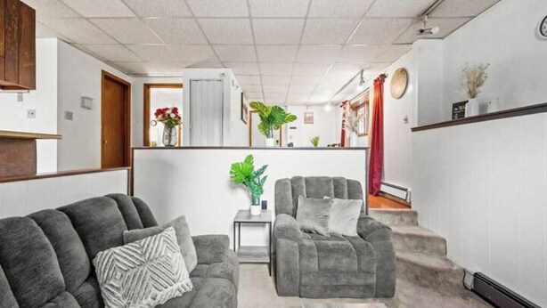 A modern living room with a grey sofa set, a small side table with a plant, and a staircase leading to an upper level. - Alaska Rafiki - Unit 3 (Fairbanks)