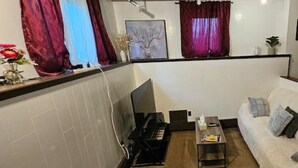 A living room with a sofa, a coffee table, a TV, and a kitchen area with a microwave. - Alaska Rafiki - Unit 3 (Fairbanks)