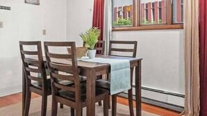 A dining area with a table and four chairs, a potted plant, and a view through a window with red curtains. - Alaska Rafiki - Unit 3 (Fairbanks)