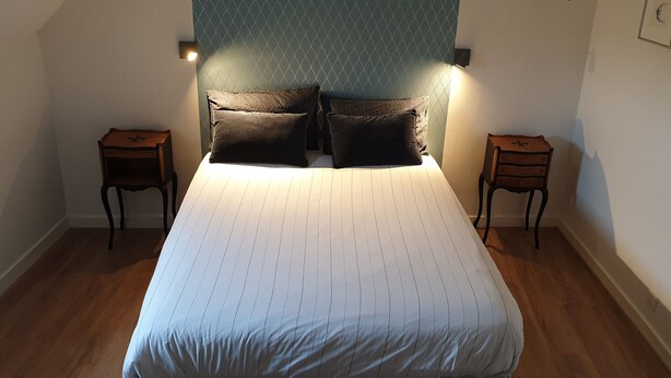 Una cama bien tendida con un edredón a rayas, dos mesitas de noche y una lámpara de pared.