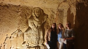 Una figura de piedra tallada en una cueva, con turistas de pie a su lado.
