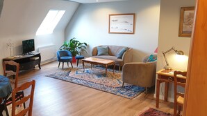 Una sala de estar acogedora con un sofá, un sillón, una mesa de centro y un televisor sobre un mueble de madera.