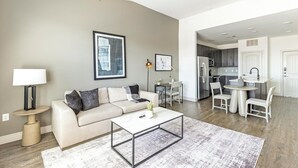 A modern living room with a sofa, coffee table, and a dining area with chairs and a table. - Landing | Beautiful 1BD, Clubhouse, Courtyard (Denton)