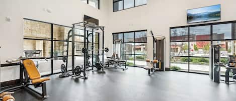 Un gimnasio espacioso con diversos equipos de ejercicio, ventanas amplias y vistas al exterior.