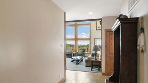 A spacious hallway leading to a living area with large windows, a wooden door, and a view of the outdoors.