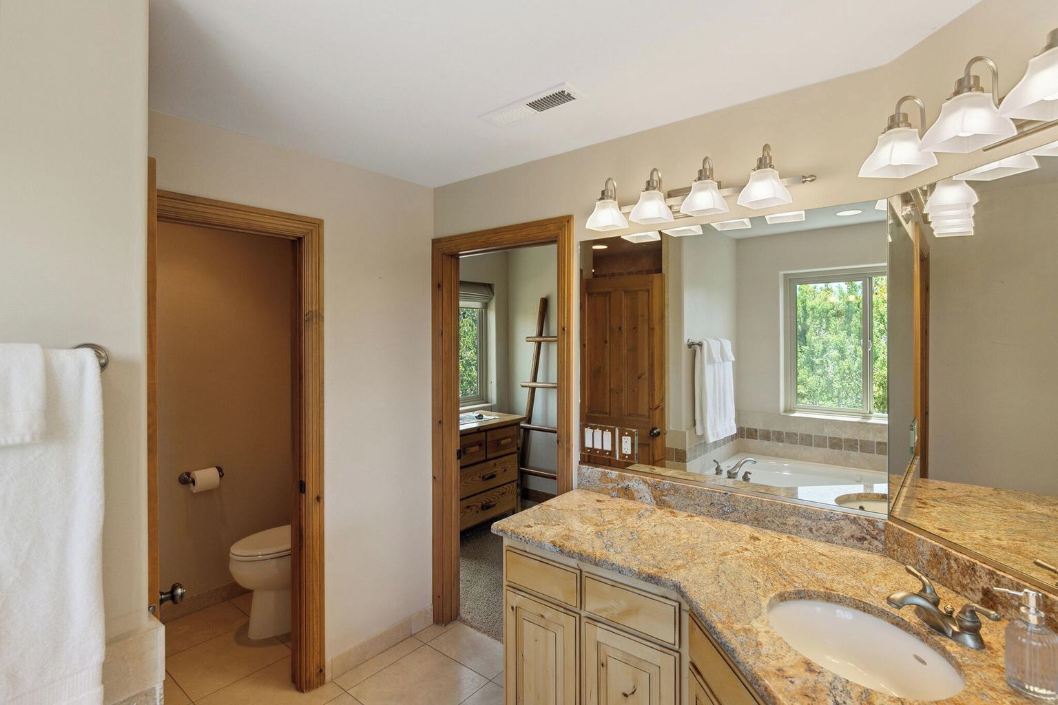 A bathroom with a granite countertop, a sink, a large mirror, and a window.