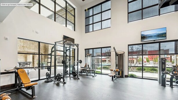 Ein geräumiges Fitnessstudio mit unterschiedlichen Trainingsgeräten, großen Fenstern und Blick ins Freie.