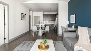 A modern living room with a grey sofa, a coffee table with a plant, and a dining area with a white table and chairs.