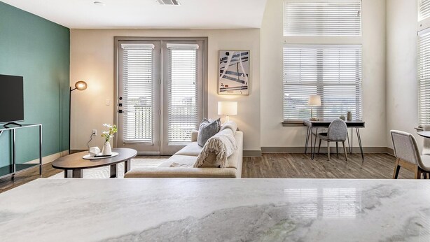 Un salon moderne avec un sol en marbre, un canapé, un coin repas comprenant une table et des chaises, et un téléviseur posé sur un meuble.
