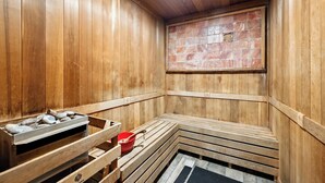 Un sauna avec des murs en bois, un banc, un plateau en pierre et un seau rouge.