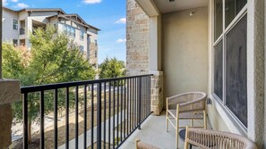 A balcony with a stone wall, a metal railing, and wicker chairs. - Landing | Modern 2BD, Clubhouse, Gym (Denton)