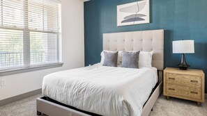 A bedroom with a bed, a nightstand, a lamp, and a window with blinds. - Landing | Chic 2BD, Gym, Clubhouse (Denton)