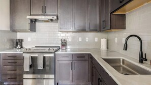 A modern kitchen with grey cabinets, a stainless steel range, a built-in oven, a coffee maker, and a black faucet. - Landing | Modern 2BD, Clubhouse, Gym (Denton)