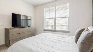 A bedroom with a bed, a TV on a dresser, and a window with blinds. - Landing | Modern 2BD, Clubhouse, Gym (Denton)
