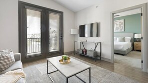 A modern hotel room with a large bed, a TV, a desk, and a balcony with blinds. - Landing | Incredible 2BD, Clubhouse, Courtyard (Denton)