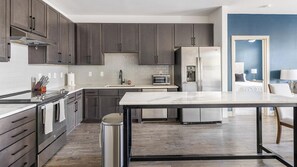 A modern kitchen with dark cabinets, a stainless steel refrigerator, and a marble countertop. - Landing | Chic 2BD, Gym, Clubhouse (Denton)