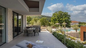Eine moderne Außenterrasse mit Essbereich, Grill und Blick auf Pool und Hügel.
