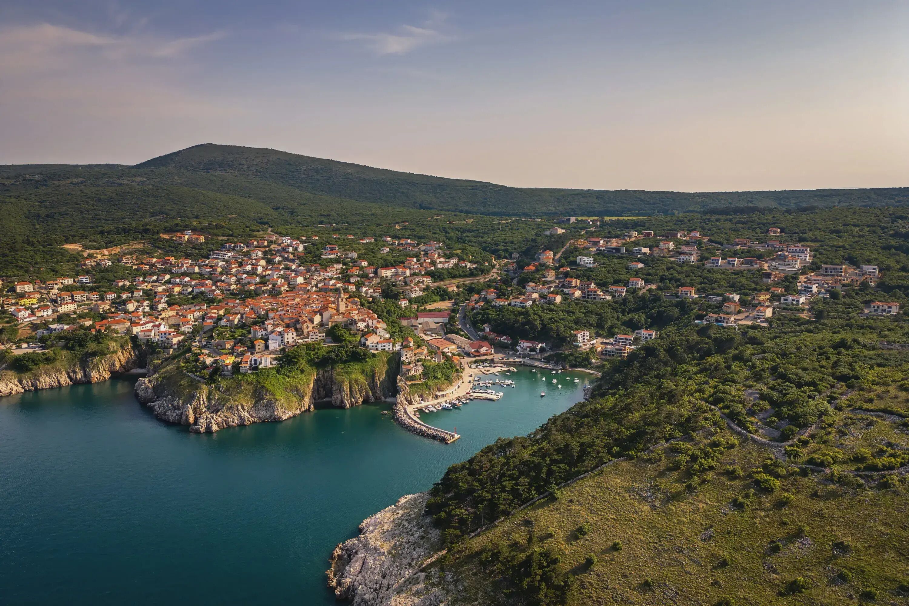 Un pueblo costero con edificios agrupados alrededor de una bahía, rodeado de colinas.