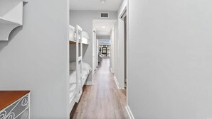Un pasillo estrecho con paredes blancas y suelo de madera, que conduce a una habitación con cama y ventana.