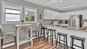 A modern kitchen with white cabinetry, a wooden countertop, and a built-in island with bar stools. - 421 N. New River Units A and B (surf city)