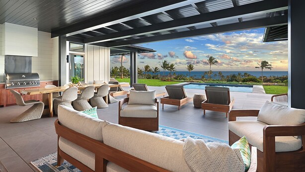 A modern outdoor living area with a pool, wooden furniture, and a view of the ocean.