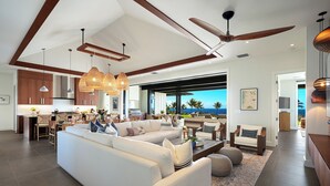 A spacious living area with a large white sofa, a dining table, and a kitchen in the background.