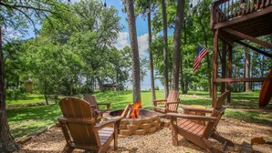 A fire pit with wooden chairs, surrounded by trees and a flag.