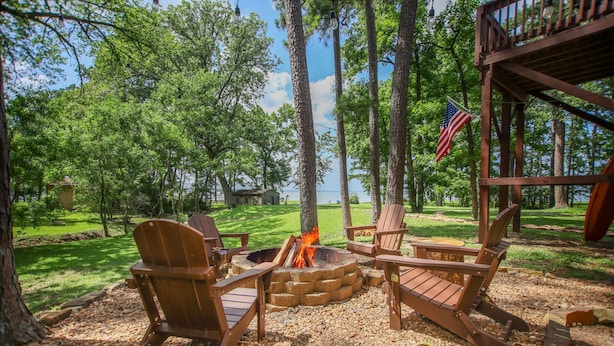 A fire pit with wooden chairs, surrounded by trees and a flag. - New Listing - Cape Royale Tree House w/ Fire Pit – Direct Lake Access (Coldspring)